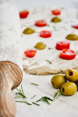Obraz na płótnie Canvas Close up olives on the white wooden table next to the raw dough with cherry tomatoes and rosemary leaves.
