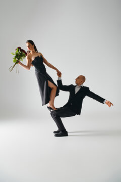 man lifting young elegant woman in black dress holding red roses and balancing during performance