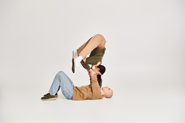 young brunette woman in casual attire balancing on hands of strong man, couple of acrobats in studio