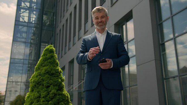 Happy smiling Caucasian businessman in city old senior mature business employer retired man entrepreneur with mobile phone using smartphone showing welcome gesture come here symbol motivation outdoors