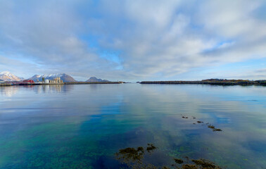 Seafood processing plant by the breakwater that separates the bay and the open sea. Snow-capped mountains and islets in the background. Lofoten Islands, Northern Norway. 