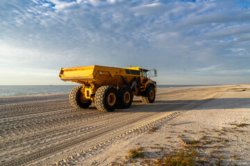 Articulated hauler mining type dump truck, in motion, carrying sand for a restoration project on a beach in the morning sun, Sanibel Island, Florida