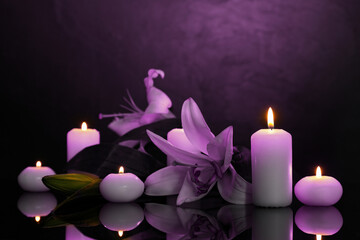 Violet lilies and burning candles on black mirror surface in darkness. Funeral attributes