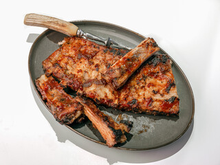 Slab of Barbecue Smoked Pork spareribs on a gray platter with a large chefs fork against a clean white background with copy space.