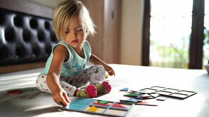 Little girl collects colorful puzzles and puts them in a book. High quality 4k footage