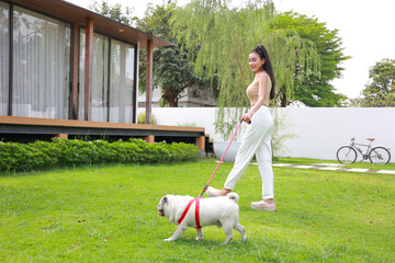 Elegant woman in white attire walking with a pug on a lush lawn near modern home