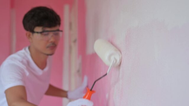 Asian male painting white wall with paint roller brush Asian man painting wall with roller and renovating home repair and interior decoration concept.