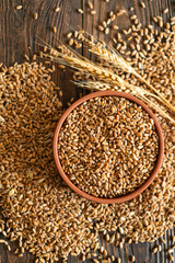 Ears of wheat and bowl of wheat grains on brown wooden background. Concept of agriculture and farming of wheat and bread.