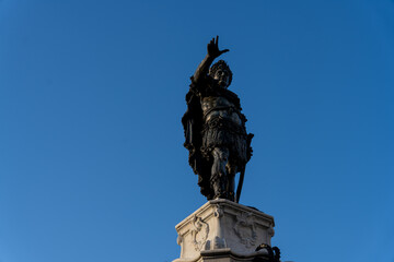 A statue of a man with a sword is standing on a pedestal in front of a blue sky