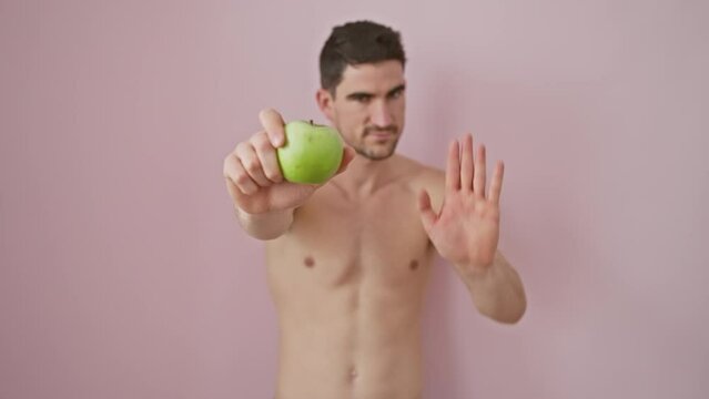 Cheerful shirtless hispanic man holding an apple over a pink isolated background, a confident gesture of health and gratefulness