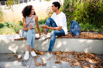 Photo of cheerful nice people best friends sitting on bench speaking about college spending time together outdoors