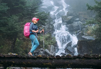Photo sur Plexiglas Makalu Young woman with backpack and trekking poles crossing wooden bridge near power mountain river waterfall during Makalu Barun National Park trek in Nepal. Mountain hiking and active people concept image