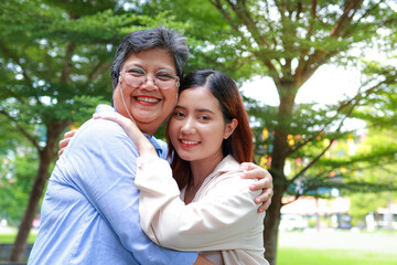 Obraz premium An elderly mother hugs her daughter, both smiling happily in the garden outside. Family concept. Health insurance