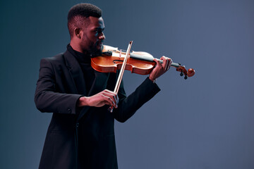 Elegant african american man in suit playing violin on dark background, creating beautiful music...
