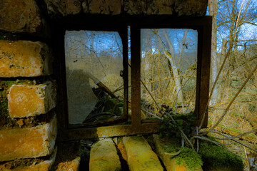 Altes zerbrochenes Fenster an einer zerstörten Backsteinruine mit Blick auf Bäume