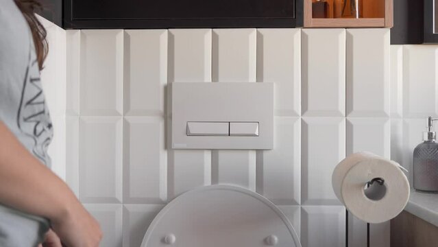 A woman presses the flush button in the toilet. Daily morning sanitary and hygienic procedures when visiting the toilet. Natural basic human needs.