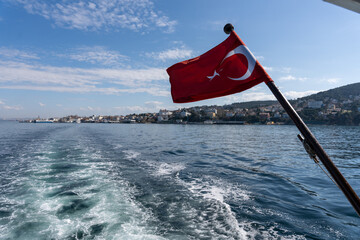 A red flag with a crescent moon on it is flying on a boat in the ocean