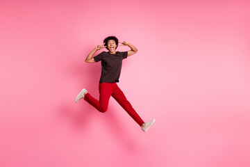 Full body length photo of young funny curly hair sportive guy jumping trampoline showing double v...