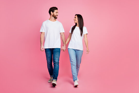 Full size photo of attractive young couple hold hands walk look each other wear trendy white clothes isolated on pink color background