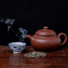 tea pot with steam on black bacground with tea leaves on wooden table