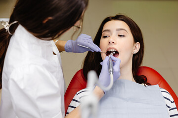 Teeth health concept. Attractive girl opening mouth under treatment at dental clinic and dentist woman doing treatment her teeth