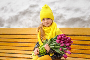 Portrait of a little toddler girl with a bouquet of yellow tulips sitting on a park bench. Spring, March 8, International Women's Day.