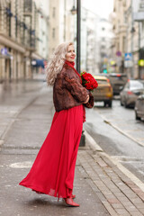 An elegant blonde in a red evening dress and fur coat is standing on the streets of the city, waiting for a taxi. Spring concept, international women's day. March 8