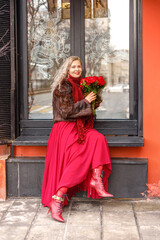 Elegant blonde in a red evening dress and fur coat on the streets. Spring concept, international...