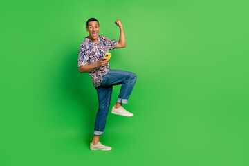 Fototapeta na wymiar Photo of positive overjoyed man stylish summer print clothes raise hand fist scream yes special offer isolated on green color background