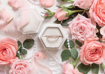Engagement ring in a a box between light pink roses and buds top view, wedding concept