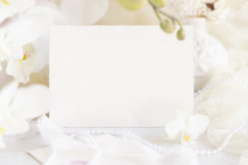 Card near white orchid flowers and decor close up, pastel romantic wedding mockup