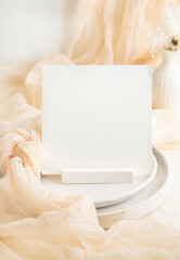 Square card near cream tulle fabric on plates close up, copy space, wedding stationery mockup