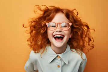 Happy laughing girl child with red hair and eyeglasses in front of orange studio background