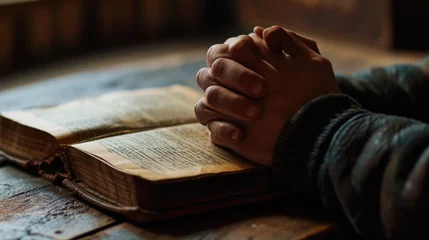 Papier Peint photo Vielles portes Person's hands folded in prayer over an open, well-worn bible, resting on a wooden table