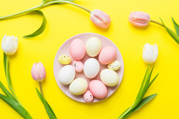 Happy Easter composition. Easter eggs in basket on colored table with yellow Tulips. Natural dyed colorful eggs background top view with copy space
