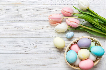 Happy Easter composition. Easter eggs in basket on colored table with yellow Tulips. Natural dyed colorful eggs background top view with copy space