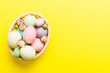 Happy Easter. Easter eggs in basket on colored table with yellow roses. Natural dyed colorful eggs background top view with copy space