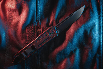 Close-up photo of a automatic folding knife on a leather jacket. - obrazy, fototapety, plakaty