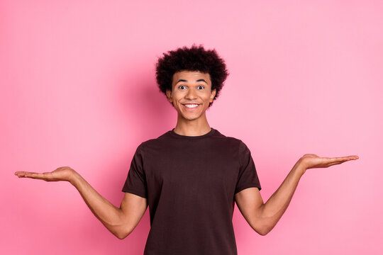 Photo of optimistic man in stylish brown t shirt choose alternatives compare same price products isolated on pink color background