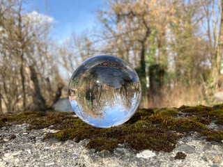 753099835 Glaskugel im Moos Spiegelt Fluss