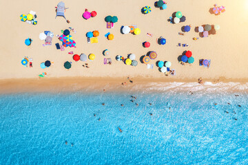 Aerial view of colorful umbrellas on white sandy beach, people in blue sea at sunset in summer....