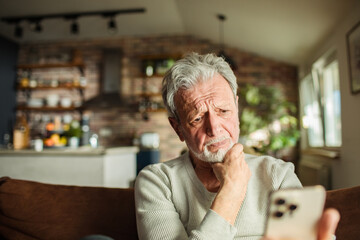 Worried senior man with smartphone on the couch at home