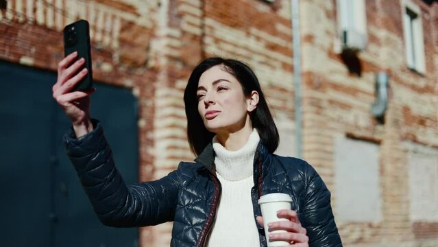 Concerned female in white turtleneck looking for right angle while taking picture with white coffee cup. Attractive woman posing for frontal cam and catching best lightning for new profile picture.