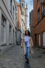 The image captures a poised African woman enjoying a leisurely walk along a cobblestone lane in a...
