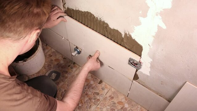 male builder glues light tiles to the wall in the bathroom
