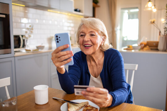 Senior woman using smartphone and credit card for online payment at home