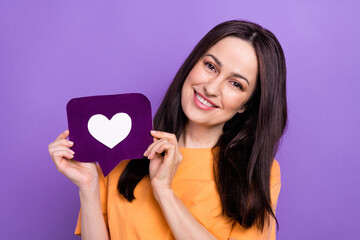 Photo of nice cheerful woman with straight hairstyle dressed orange t-shirt demonstrate heart icon isolated on purple color background