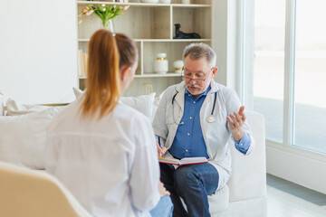 Senior man doctor examining young woman in doctor office or at home. Girl patient and doctor have consultation in hospital room. Medicine healthcare medical checkup. Visit to doctor