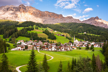 Mountain village with a church in Dolomite alps in summer among green meadows