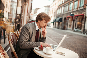 Mature man using a laptop while enjoying coffee in an outdoor cafe